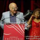 Tom Joyner speaks at the podium while Wife Denise Richards looks on at Essence Evening of Excellence