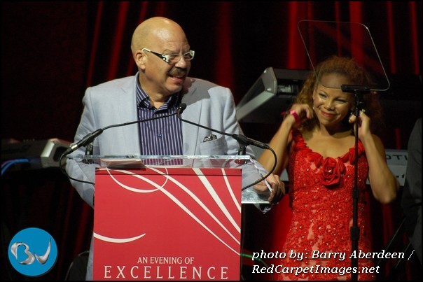 Tom Joyner speaks at the podium while Wife Denise Richards looks on at Essence Evening of Excellence